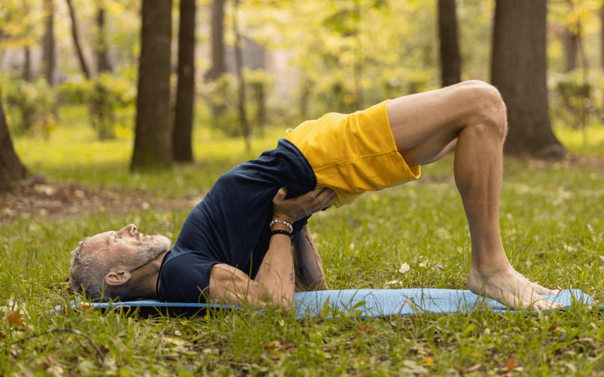 Beckenbodentraining Übungen Mann. Symbolbild: Ein Mann macht eine Übung auf einer Turnmatte im Grünen. Englisch: Pelvic floor exercises for men. Symbolic image: a man is doing an exercise on a gym mat in a green space.
