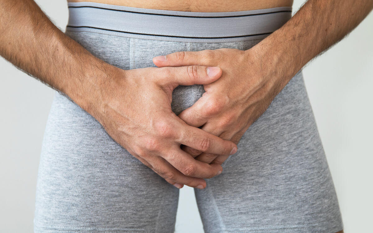 Beschneidung Symbolbild: Bildausschnitt eines männlichen Genitalbereichs in Unterhose, bei dem die Hände vor das Geschlechtsteil gelegt sind. Englisch: Circumcision Symbolic image: detail of a male genital area in underpants, with the hands placed in front of the genitals.