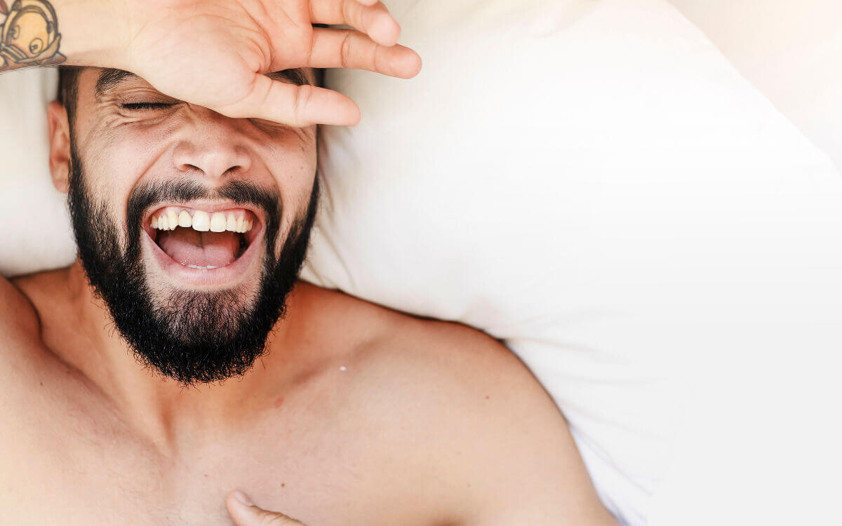 Ist Masturbieren gesund? Symbolbild: Gesicht eines Mannes, der sehr glücklich im Bett liegt. Is masturbation healthy? Symbolic image: Face of a man lying very happily in bed.