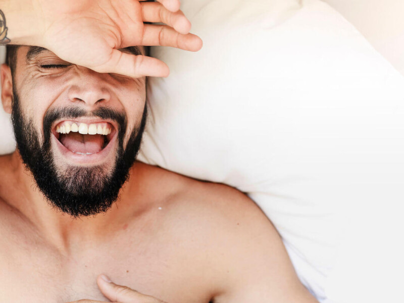Ist Masturbieren gesund? Symbolbild: Gesicht eines Mannes, der sehr glücklich im Bett liegt. Is masturbation healthy? Symbolic image: Face of a man lying very happily in bed.
