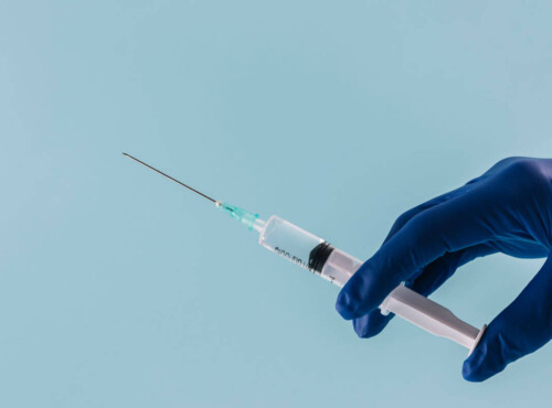 Spritze in den Penis. Symbolbild: Eine Hand mit medizinischem Handschuh hält eine Spritze. Englisch: Penis Injection. Symbolic image: A hand wearing a medical glove holding a syringe.