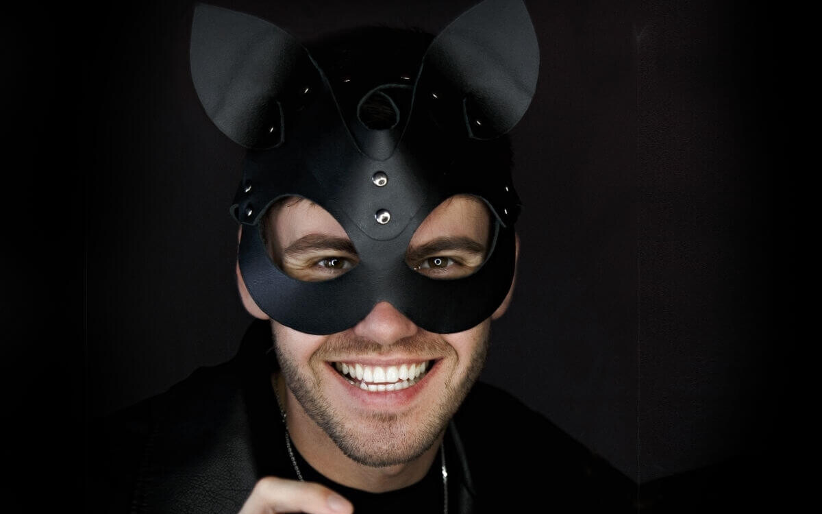 Kittenplay Symbolbild: Mann mit schwarzer Katzenmaske lächelt in die Kamera. . Kitten play Symbolic image: Man wearing a black cat mask smiles at the camera.