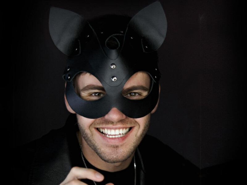 Kittenplay Symbolbild: Mann mit schwarzer Katzenmaske lächelt in die Kamera. . Kitten play Symbolic image: Man wearing a black cat mask smiles at the camera.