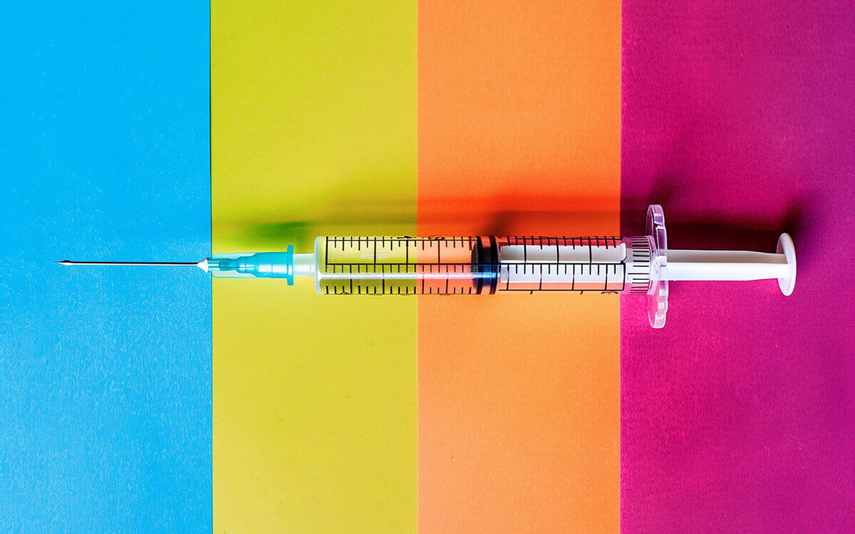 Impfungen für Männer Symbolbild: Eine Spritze liegt auf einem bunt gestreiften Hintergrund. Vaccinations for men Symbolic image: A syringe lies on a colorful striped background.