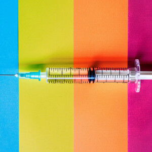 Impfungen für Männer Symbolbild: Eine Spritze liegt auf einem bunt gestreiften Hintergrund. Vaccinations for men Symbolic image: A syringe lies on a colorful striped background.