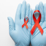 TasP Symbolbild: Zwei Hände mit medizinischen Handschuhen halten eine große und eine kleine Aids-Schleife. TasP Symbolic image: Two hands wearing medical gloves hold a large and a small AIDS ribbon.