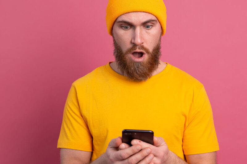 Dating Apps für Schwule und LGBTQ+-Personen. Symbolbild: Ein Mann schaut erstaunt auf sein Handy. Gay Dating apps for gay and LGBTQ+ people. Symbolic image: A man looks at his cell phone in amazement.
