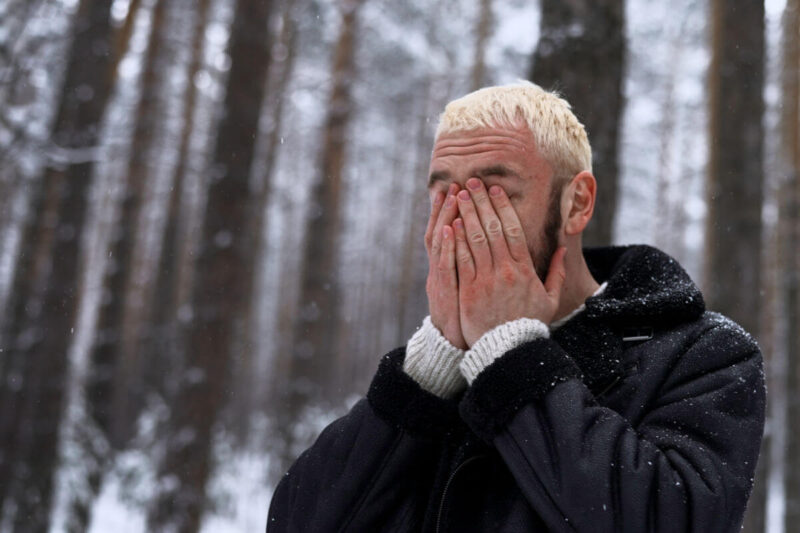 Winterdepression: eine Person läuft durch einen verschneiten Wald und hält sich die Hände vors Gesicht. Winter depression: a person walks through a snow-covered forest, covering their face with their hands.