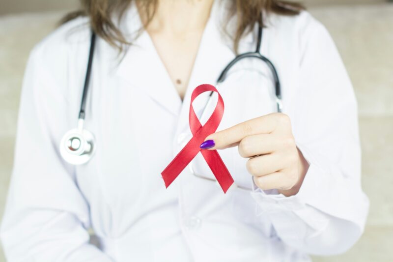 HIV-Prävention: Eine Frau in weißem Arzt-Kittel und mit Stethoskop hält die Aids-Schleife in die Kamera. HIV prevention: A woman in a white doctor's coat and stethoscope holds up the AIDS ribbon to the camera.