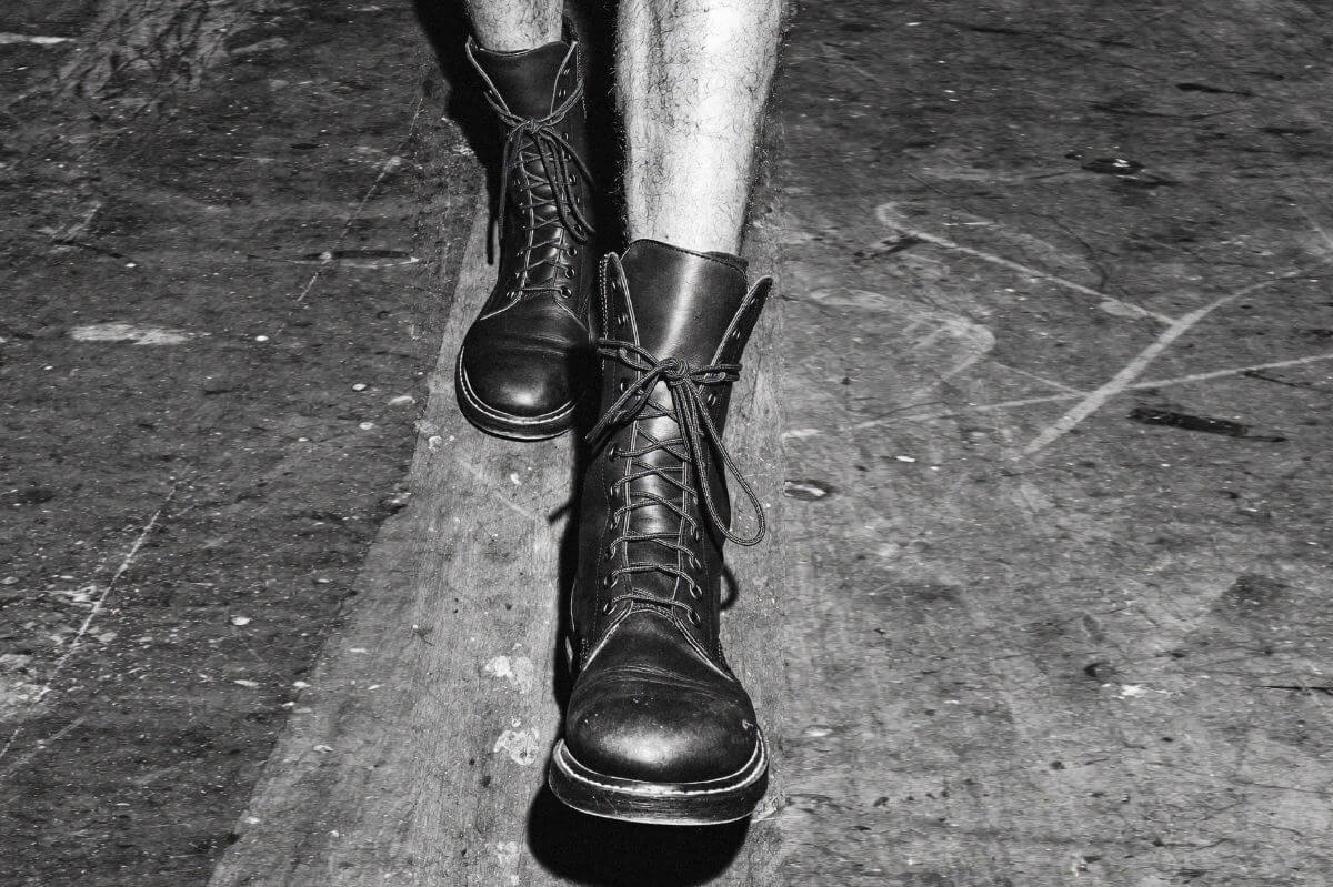 Symbolbild BDSM Dominanz Rollenspiele: Kontrolle, Macht und Führung: Schwarz-Weiß-Bild Schwere Stiefel auf Asphalt Symbolic image of BDSM dominance role-playing: control, power, and leadership: black-and-white photo of heavy boots on asphalt