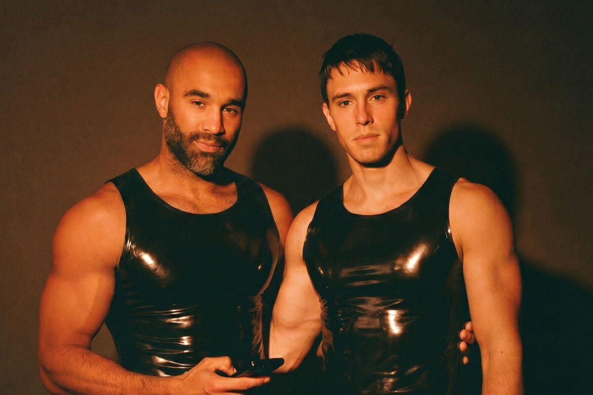 Submissive Rollen BDSM Symbolbild: Zwei Männer in Latex-Outfit schauen in die Kamera. Englisch: Submissive roles BDSM symbolic image: Two men in latex outfits looking into the camera.