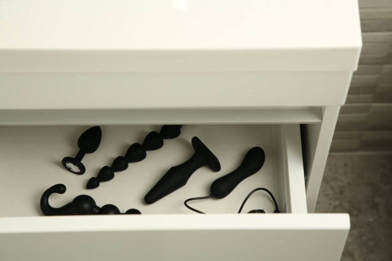 Schwarze Analtoys in einer Schublade, u. a. eine Analkette – Inspiration, um eine Analkette zu verwenden. EN: Black anal toys in a drawer, including an anal bead string – inspiration for using anal beads.