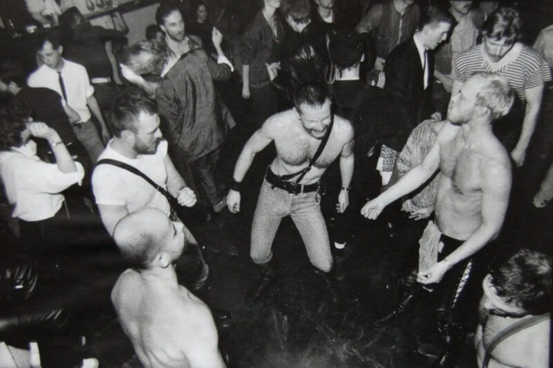 DE: Catacombs Sexclub – historische Schwarz-Weiß-Aufnahme tanzender Männer in Leather-Outfits auf der Tanzfläche der San Franciscoer Leather-Szene EN: Catacombs sex club – historical black-and-white photo of men in leather dancing on the floor of San Francisco's leather scene